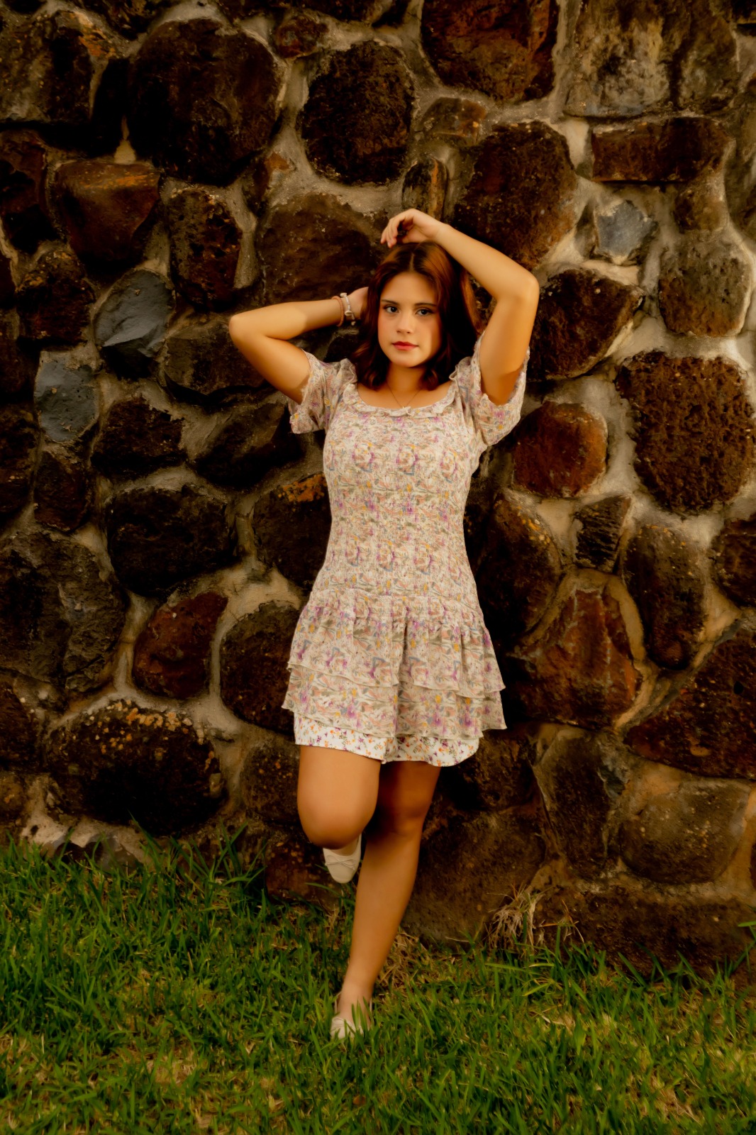 Antonella junto al muro de piedra con las manos en el cabello